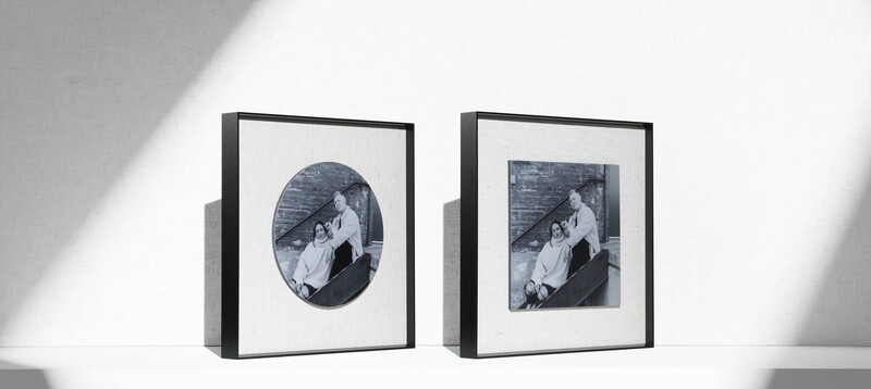 Two black-framed photographs displaying identical black and white portraits of figures seated by water.