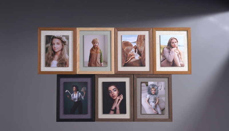 Seven framed portrait photographs arranged on a gray wall in two rows, featuring various subjects in different styles and frame finishes.