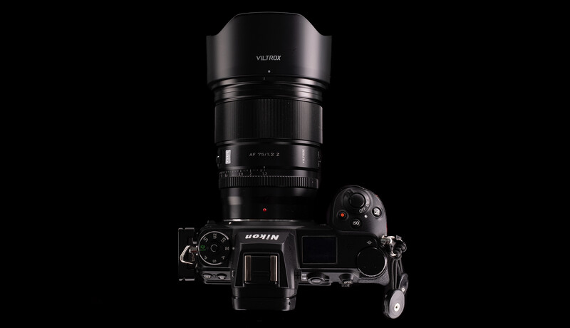 Overhead view of a mirrorless camera with attached telephoto lens and lens hood on black background.