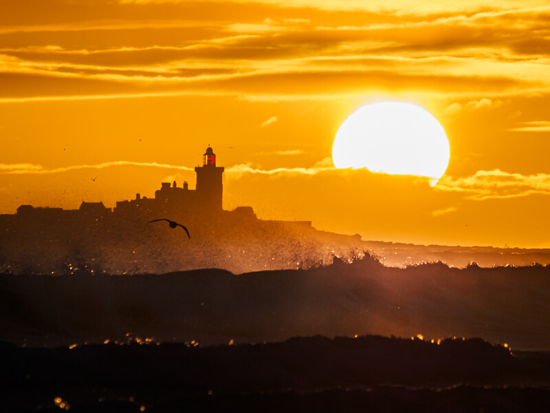 Silhouetted hilltop town with church tower against a massive golden sunset sun.