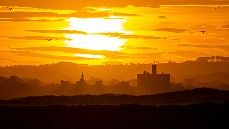 City skyline silhouetted against a brilliant golden sunset with dramatic cloud formations.