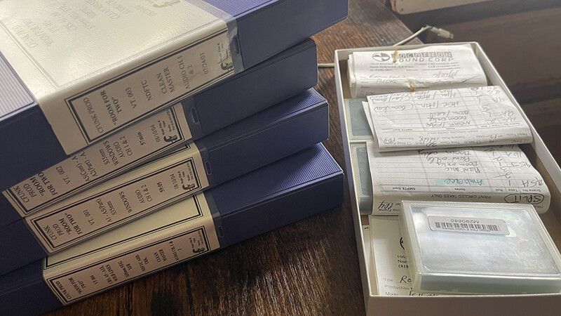 Stack of vintage bound books with worn leather spines alongside a white storage box containing organized photograph or document slides.