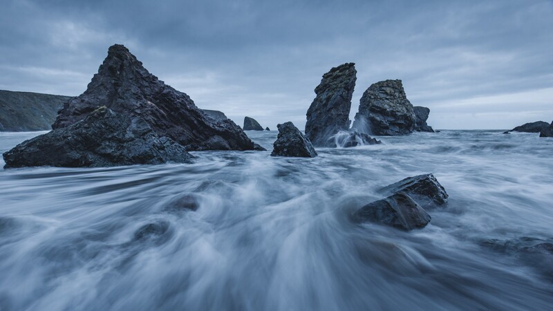 Rocky sea stacks rise from churning waves on a moody coastal beach at dusk.