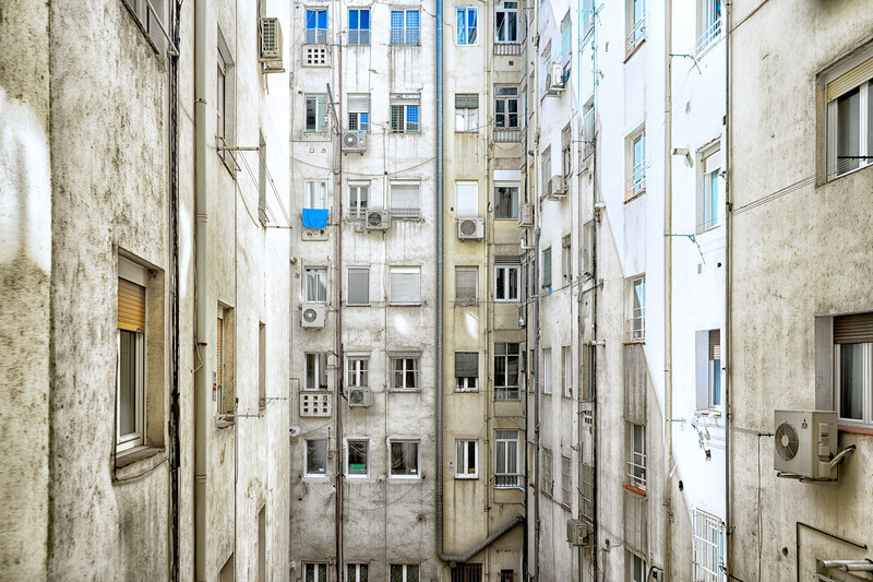 Narrow urban courtyard lined with weathered residential apartment buildings viewed from above.