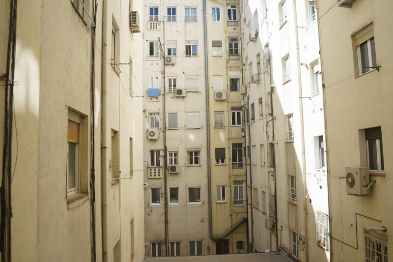 Narrow urban courtyard lined with cream and white residential buildings featuring multiple small windows and air conditioning units.