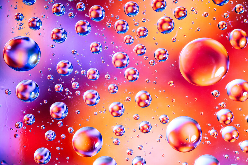 Colorful oil or soap bubbles floating against a vibrant gradient background transitioning from purple to orange and red.