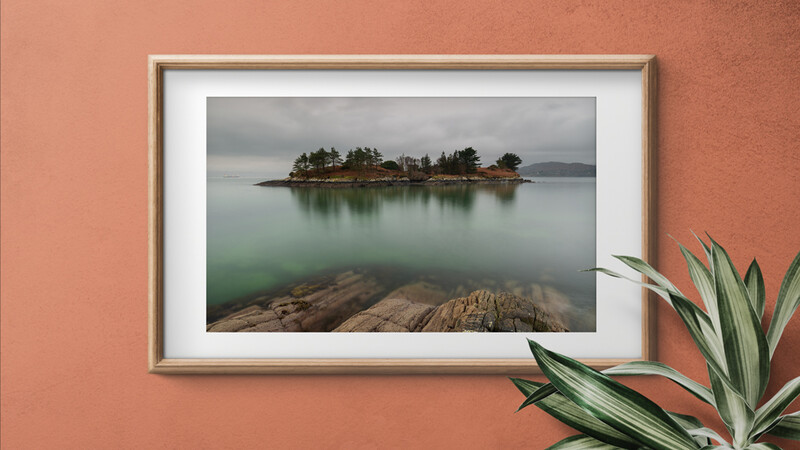 Serene lake with forested island and rocky foreground under overcast sky.