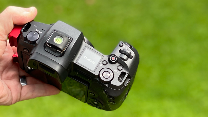 Hand holding a mirrorless camera with articulating screen and hot shoe accessory against green background.