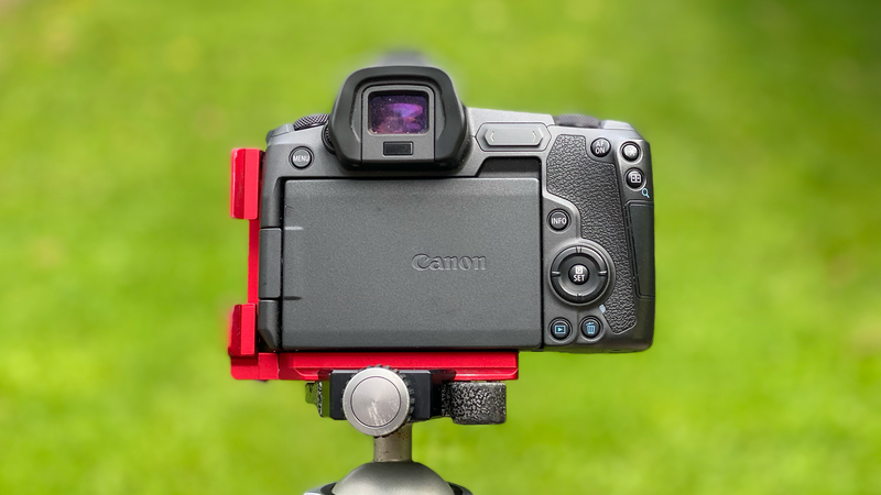 Canon mirrorless camera mounted on a tripod with red L-brackets against a blurred green background.