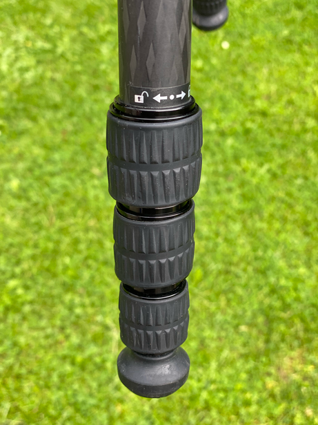 Close-up of a rubber camera grip with textured ridges wrapping around a tripod or lens barrel against a bright green bokeh background.