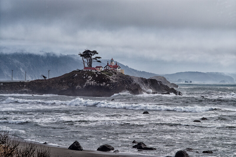 Rocky island with temple structure in turbulent ocean waters under overcast sky.