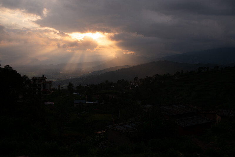 Dramatic crepuscular rays breaking through storm clouds over a mountainous valley at dusk.