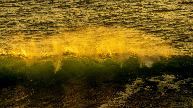 Golden-hour waves with backlit spray and foam rolling toward shore.