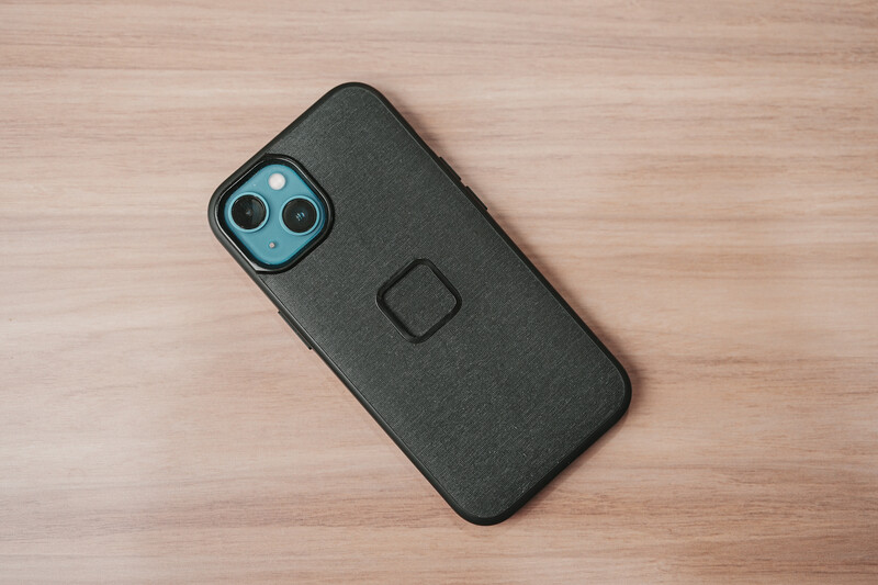 Black protective phone case with dual camera cutout and square logo detail on wooden surface.