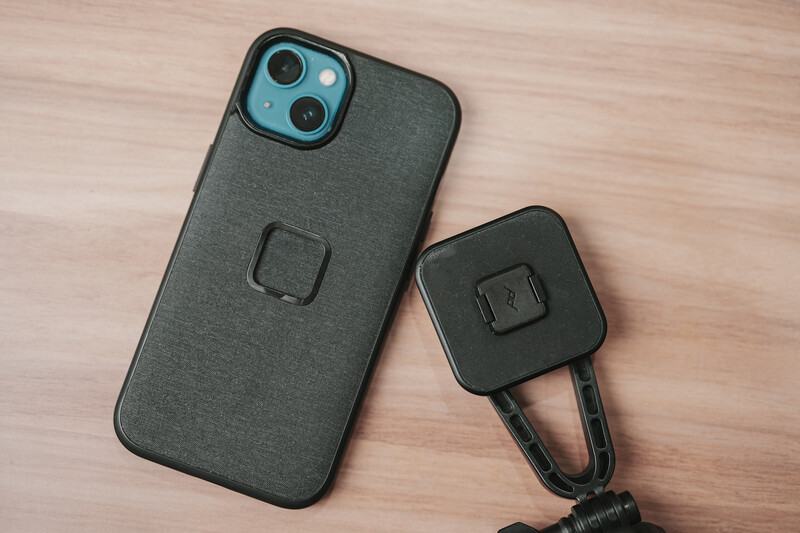 Gray fabric iPhone case with square magnetic mount next to matching black magnetic car vent mount on wooden surface.