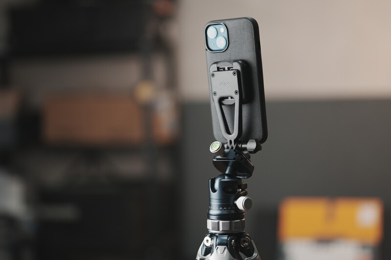 iPhone mounted on a compact tripod with ball head against a blurred interior background.