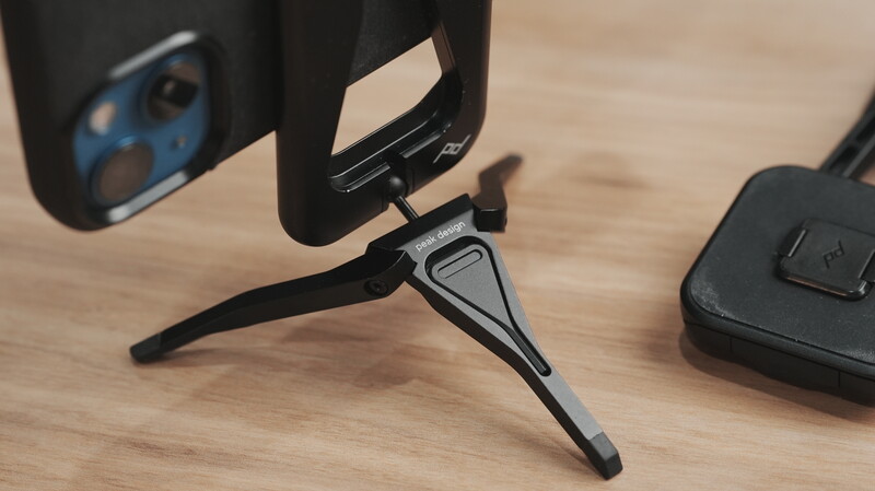 Tripod-mounted smartphone holder with legs extended on wooden surface.