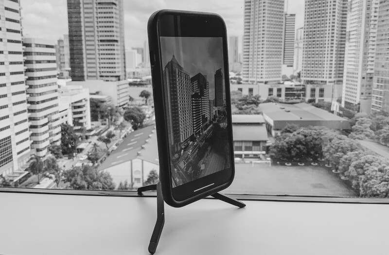 Smartphone displaying a black and white cityscape photograph, positioned on a stand with a high-rise urban skyline visible in the background.