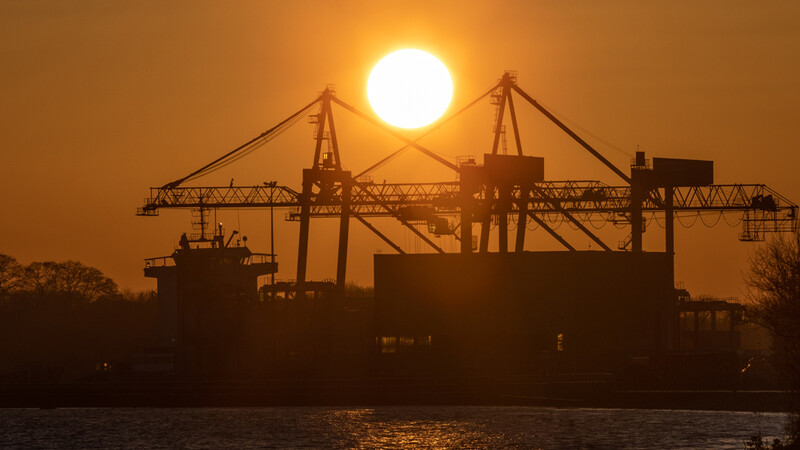 Industrial shipping port silhouetted against a large sun at sunset or sunrise.