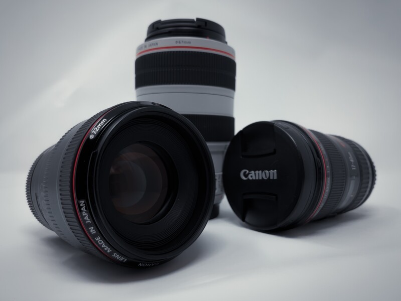 Three Canon telephoto lenses arranged on a gray surface, displaying barrel designs with red accent rings and lens caps.