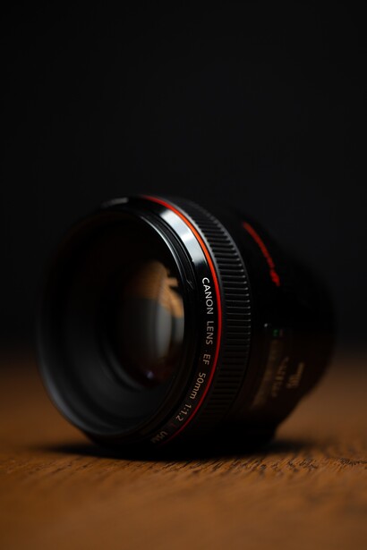 Fast prime lens with red markings positioned at an angle on a warm textured surface against a dark background.