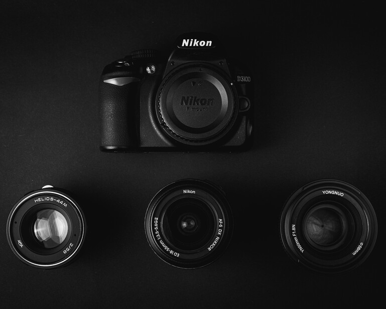 Nikon DSLR camera body with three interchangeable lenses arranged on black background.