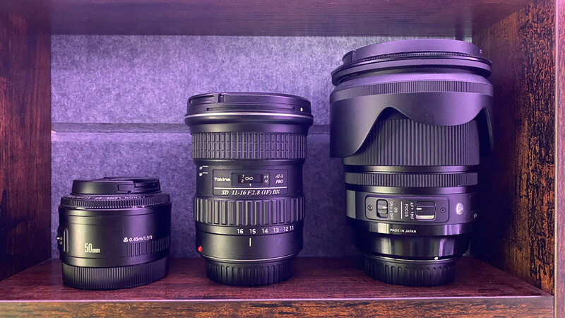 Three camera lenses of increasing size arranged left to right on a wooden shelf with purple ambient lighting.