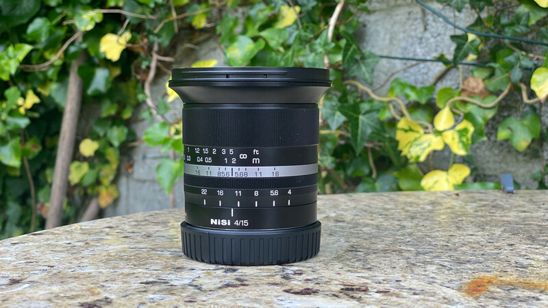 Nikon 4/15 wide-angle lens with focus and aperture rings displayed on stone surface against foliage background.
