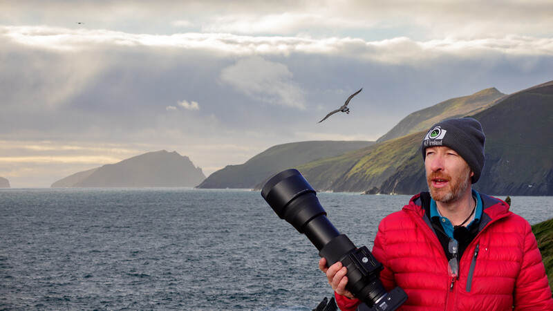 Wildlife photographer holding a telephoto lens while scanning coastal cliffs for birds.