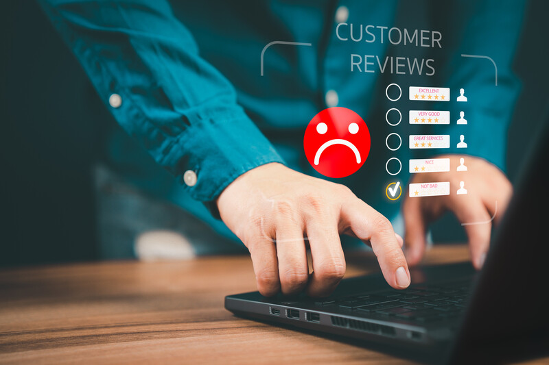 Person's hand on laptop keyboard with digital customer reviews interface overlay showing satisfaction ratings and a red sad face icon.