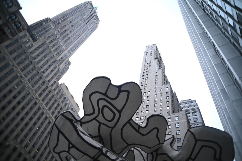 Abstract black sculptural form silhouetted against tall art deco and modern skyscrapers photographed from below.