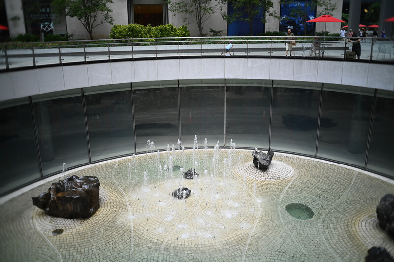 Circular zen garden with raked gravel, sculptural rocks, and a central metallic installation viewed from above through glass.
