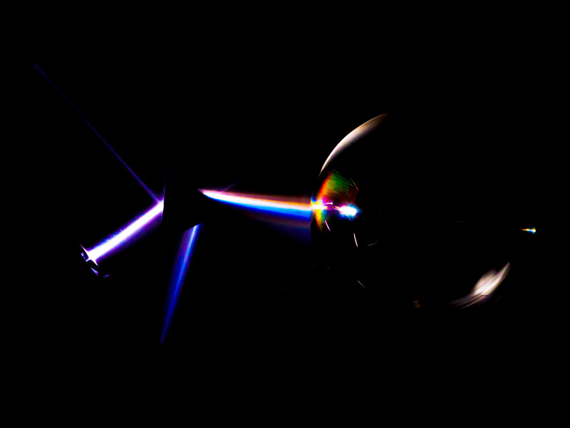 High-speed light painting photograph showing blue and magenta light trails against a black background.