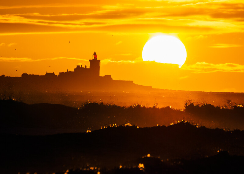 Silhouetted castle on a hilltop against a large setting sun in a golden sky at sunset.