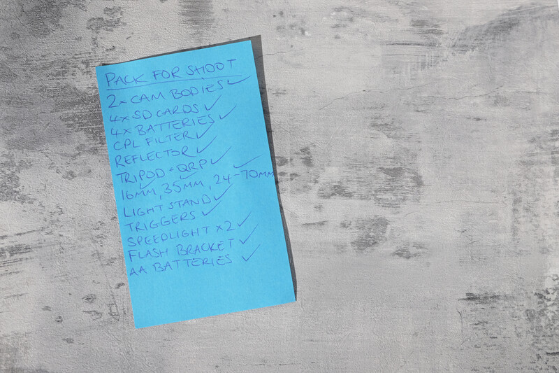 Blue sticky note with handwritten shopping list on weathered concrete surface.