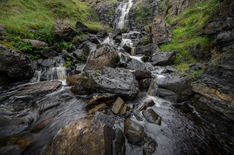 Cascading waterfall flowing over moss-covered rocks in a lush ravine.