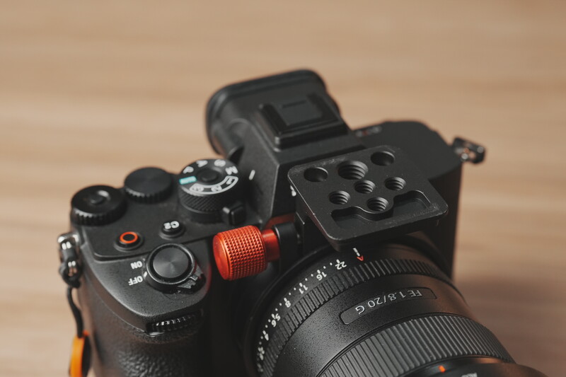 Sony mirrorless camera with red microphone and black lens on wooden surface.