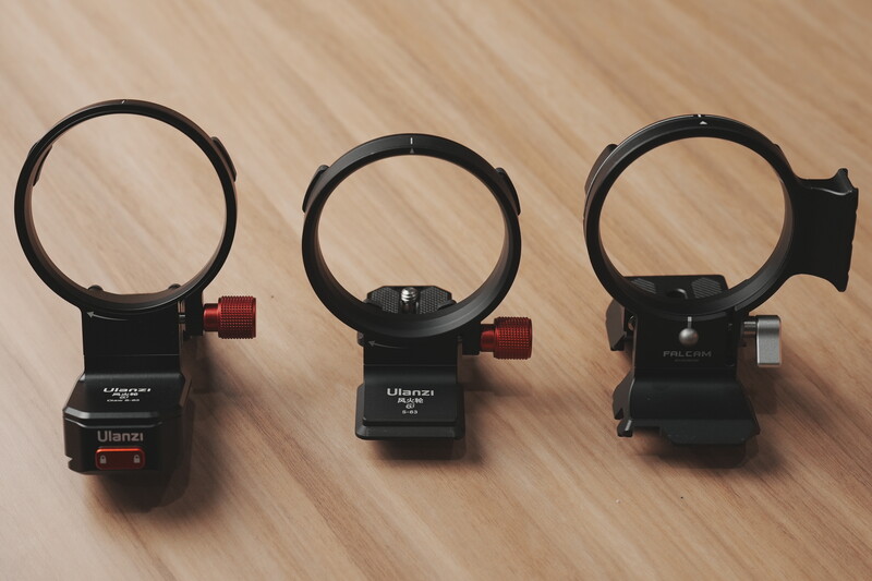 Three black camera lens collar mounts with circular rings and red adjustment knobs arranged on a wooden surface.