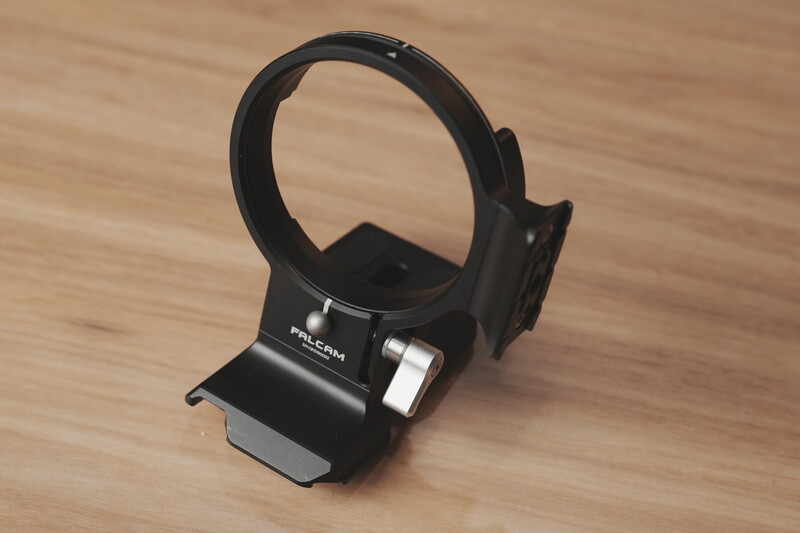 Black camera lens hood mounted on a wooden surface next to its protective stand.