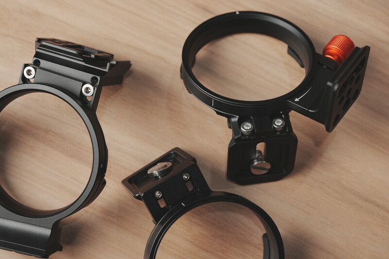 Three black camera flash brackets and light stands displayed on a wooden surface.