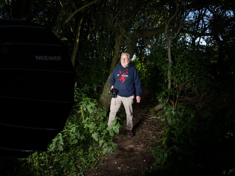 Person walking on a narrow woodland path at dusk, surrounded by dense green foliage and tree branches.