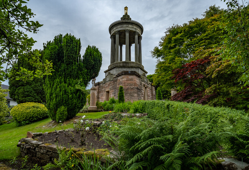 Stone tower with columned rotunda surrounded by lush green landscaping and mature trees.