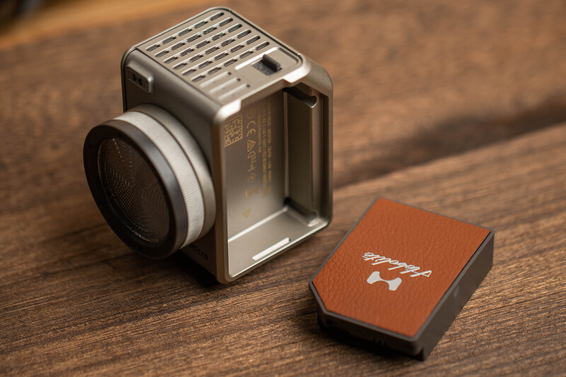 Vintage square-format camera with chrome finish and leather carrying case on wooden surface.