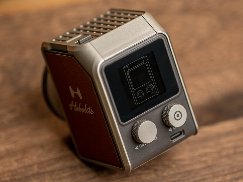 Vintage digital watch with rectangular face, dual control knobs, and metal mesh band on wooden surface.
