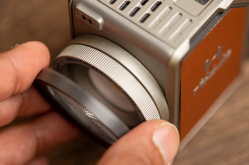 Close-up of hands holding a camera lens with a textured grip ring and focus mechanism visible.