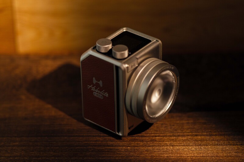 Vintage film camera with chrome lens and dark body positioned on wooden surface under warm lighting.