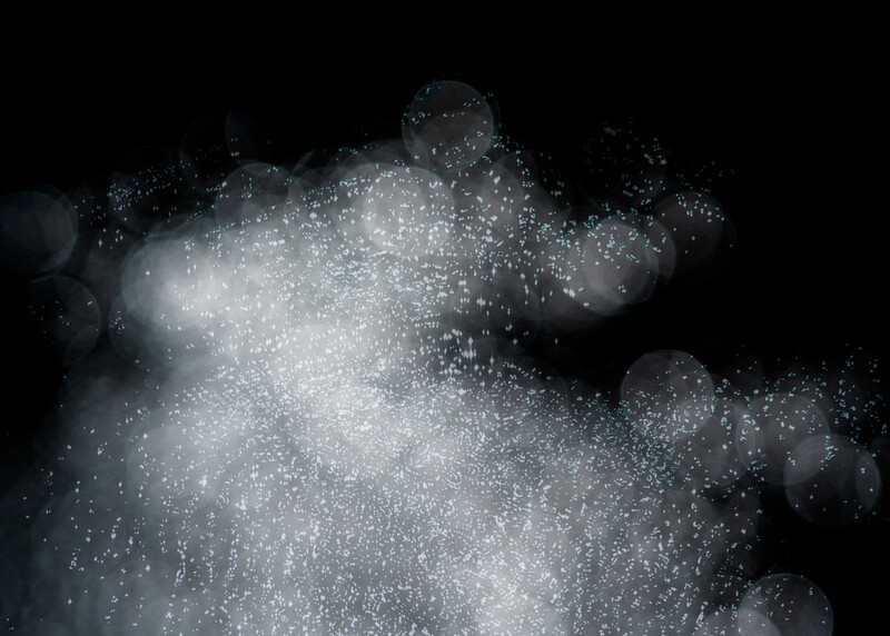 Particles dispersing through dark space in a cloud-like formation with bokeh.
