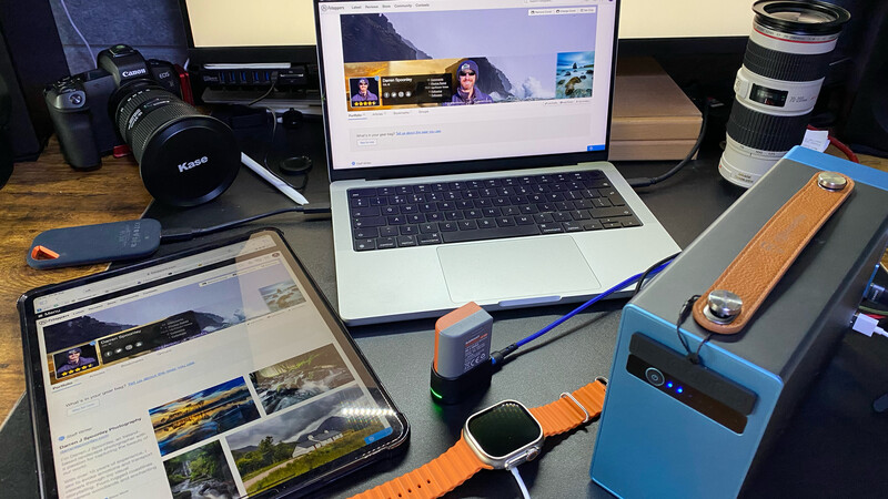 Creative professional workspace with laptop, camera gear, and smartwatch on wooden desk.