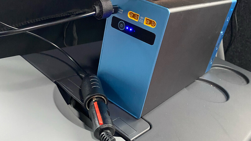 Blue portable power bank with dual USB ports and indicator lights connected to charging cables.
