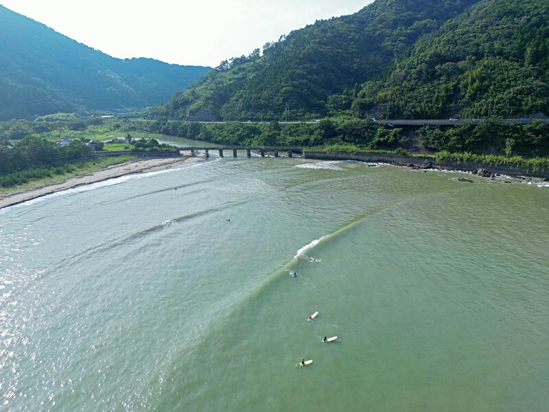 Aerial view of a wide river with pale greenish water flowing through a mountainous valley with forested slopes.